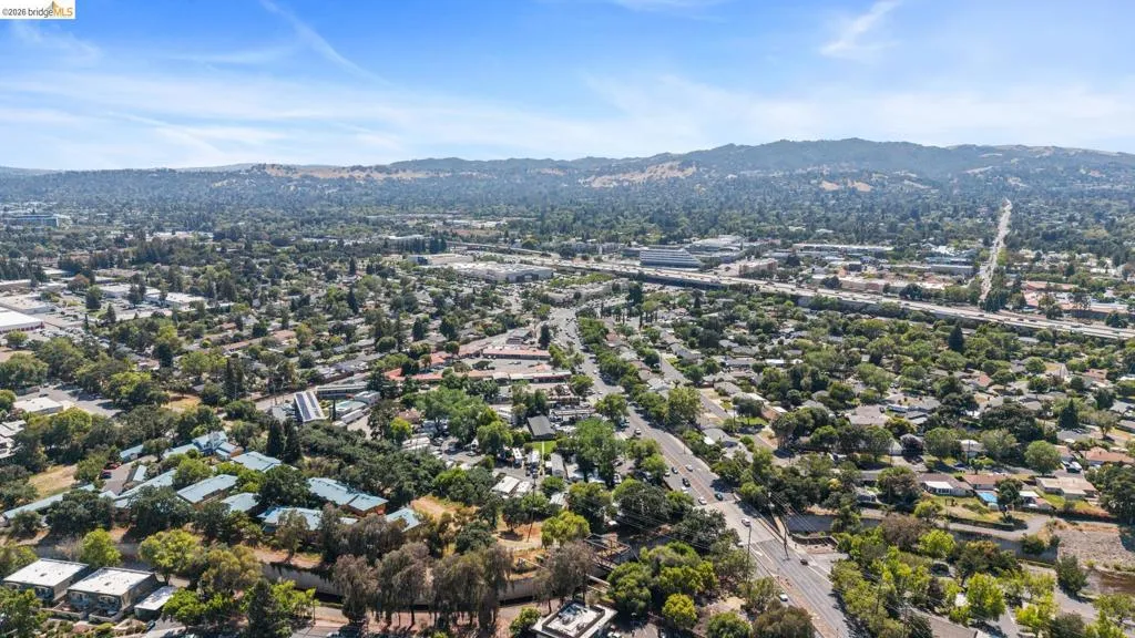 Expansive aerial encompassing a residential area with varied housing styles, mature trees, and distant hills