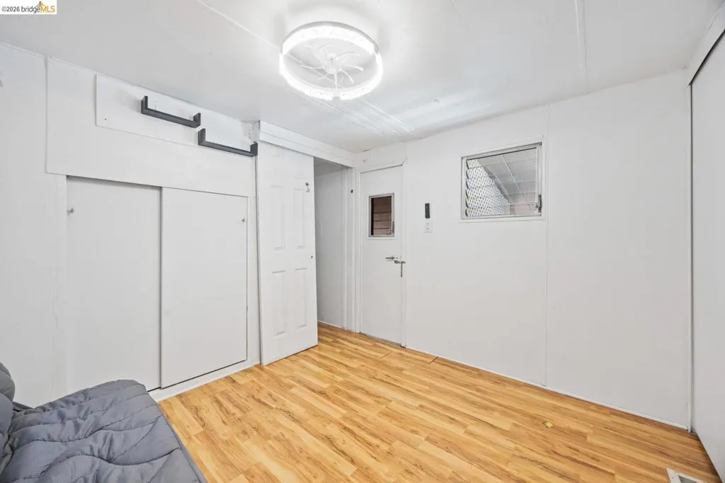 Bright interior space featuring wood-finish flooring, a contemporary ceiling light fixture, a sliding door wardrobe, a louvered window, and white paneled walls