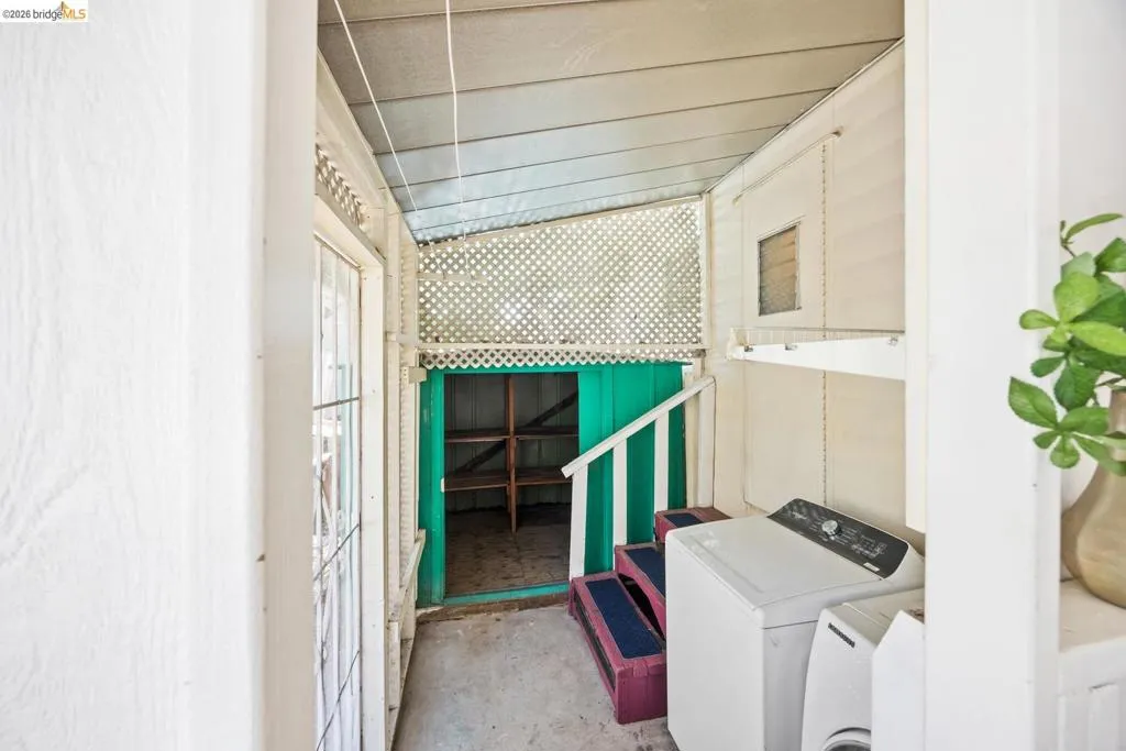 Covered outdoor utility area featuring a washer and dryer, lattice screening, and an integrated storage nook with shelving