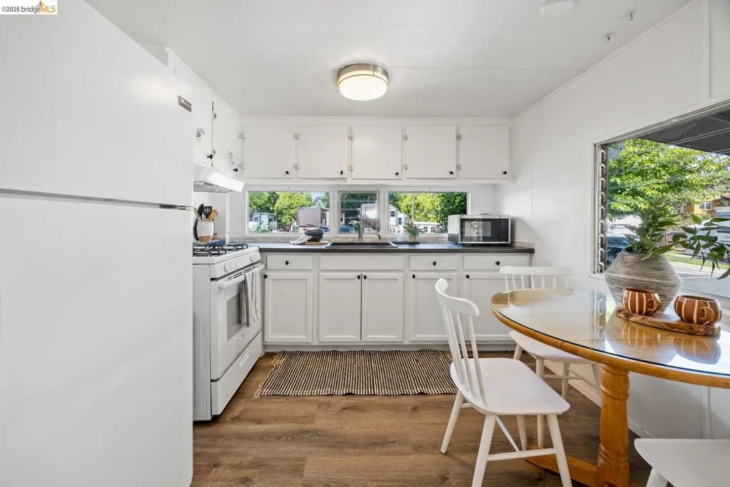 Kitchen featuring white cabinetry, dark countertops, wood-finish flooring, and white appliances