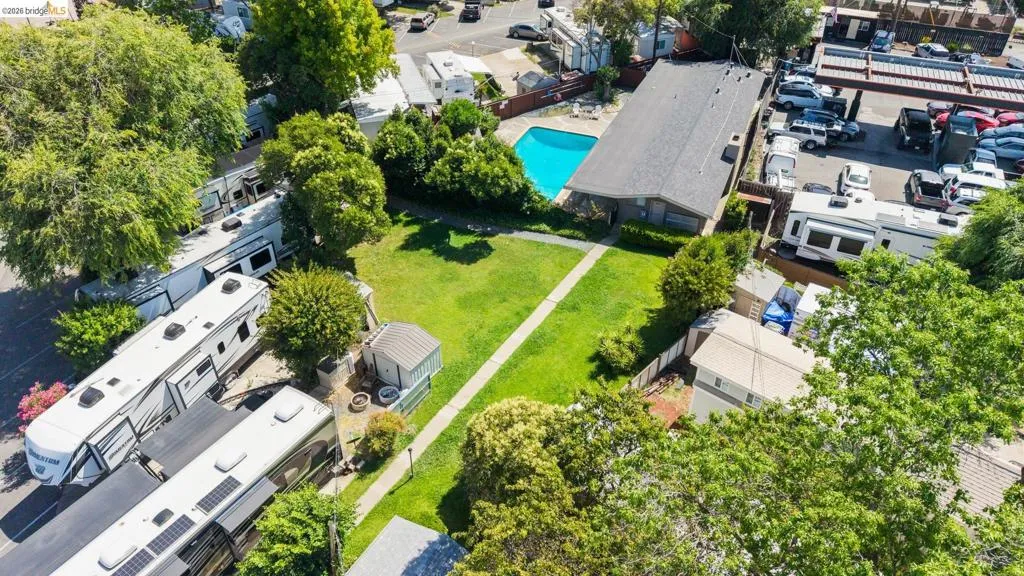 Expansive green space featuring a rectangular swimming pool, mature trees, and a paved pathway