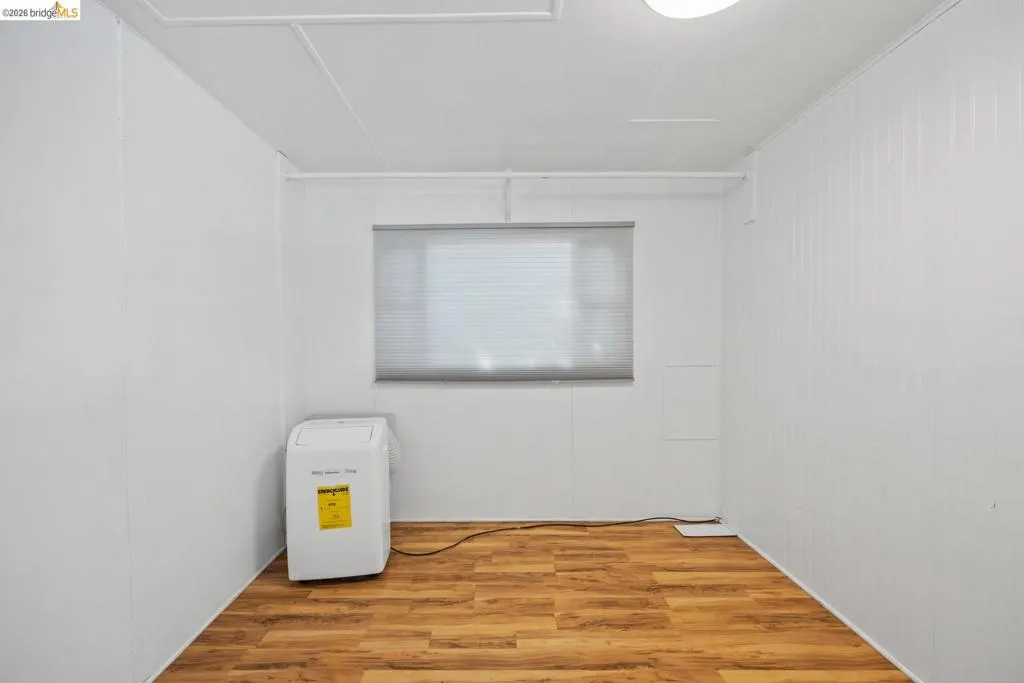 Utility space featuring wood-finish flooring, white paneling, a window with blinds, and white ceiling panels
