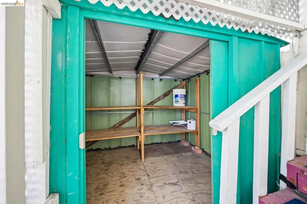 Storage shed with green painted corrugated metal walls, wood shelving, and plywood flooring
