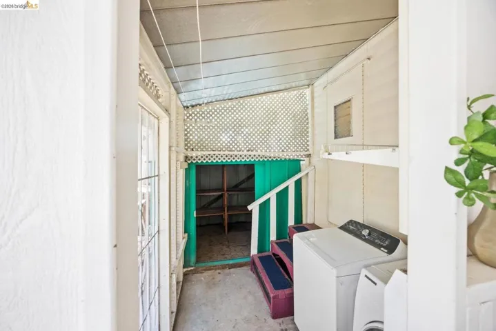 Covered outdoor utility area featuring a washer and dryer, lattice screening, and an integrated storage nook with shelving
