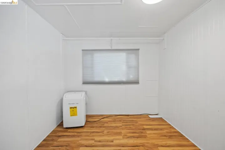 Utility space featuring wood-finish flooring, white paneling, a window with blinds, and white ceiling panels