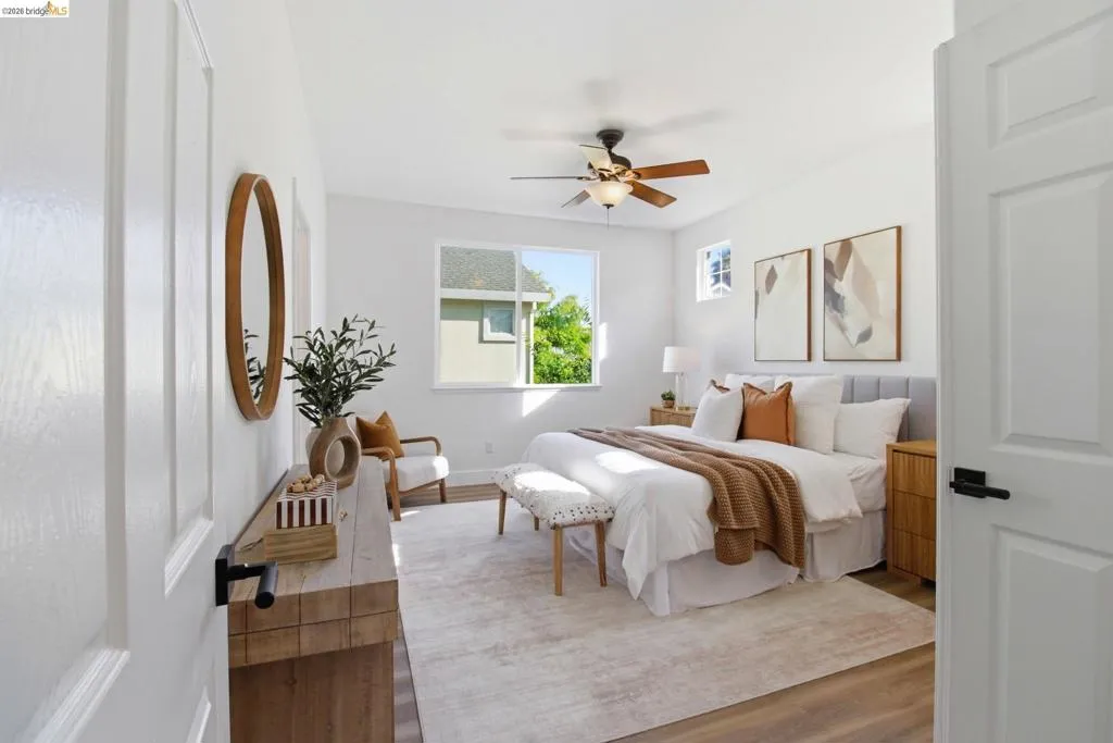 Bedroom featuring a ceiling fan with integrated lighting, multiple windows, light wood-finish flooring, and a paneled interior door with matte black hardware