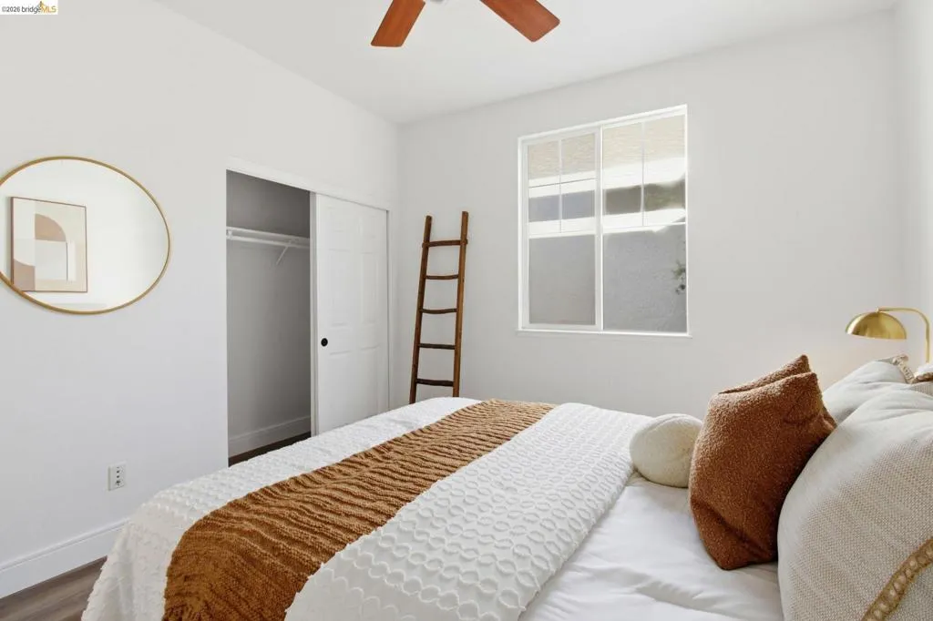 Bedroom featuring wood-finish flooring, a ceiling fan, and a window with white framing