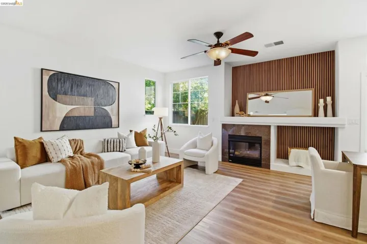 Bright living area featuring wood-finish flooring, a contemporary fireplace with a stone surround and wood slat accent wall, and a ceiling fan