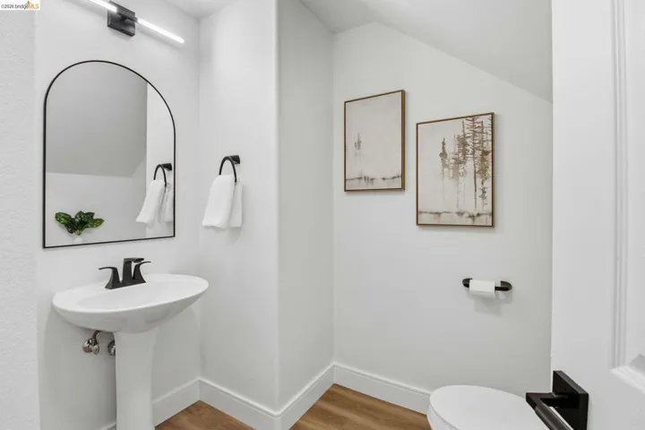 White pedestal sink with matte black faucet, framed arched mirror, and coordinating matte black light fixture
