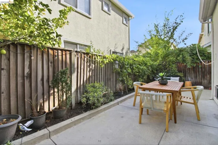 Paved patio area featuring a wooden fence with established greenery, mature trees, and a planting bed