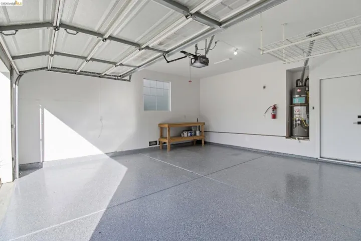 Spacious garage featuring a durable epoxy floor coating, automatic garage door opener, overhead storage rack, and a dedicated utility closet