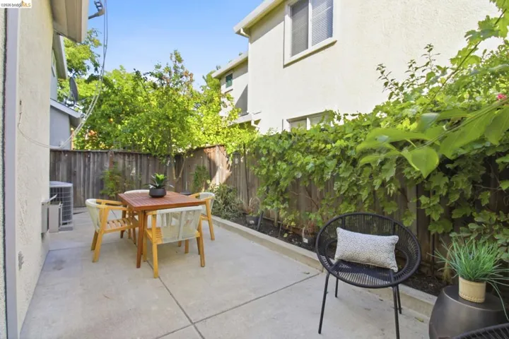Private concrete patio featuring a wood fence, mature foliage, and stucco exterior walls