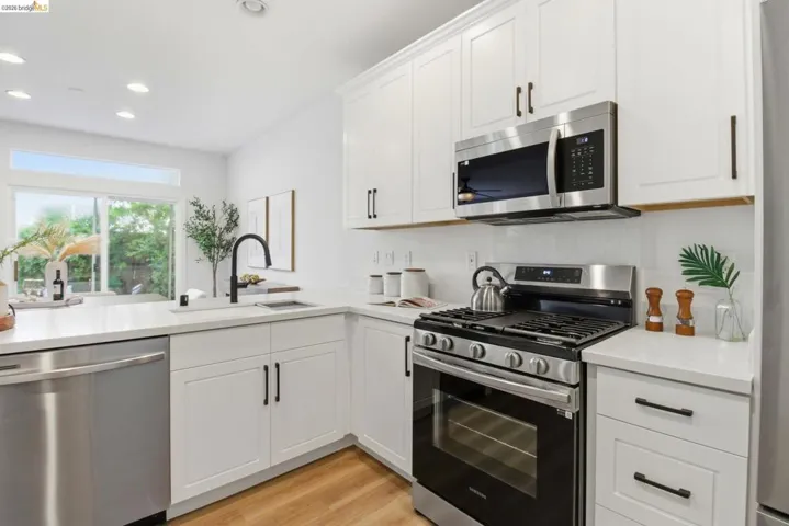 Modern kitchen featuring white shaker cabinetry, stainless steel appliances, a black gooseneck faucet, light countertops, and wood-finish flooring