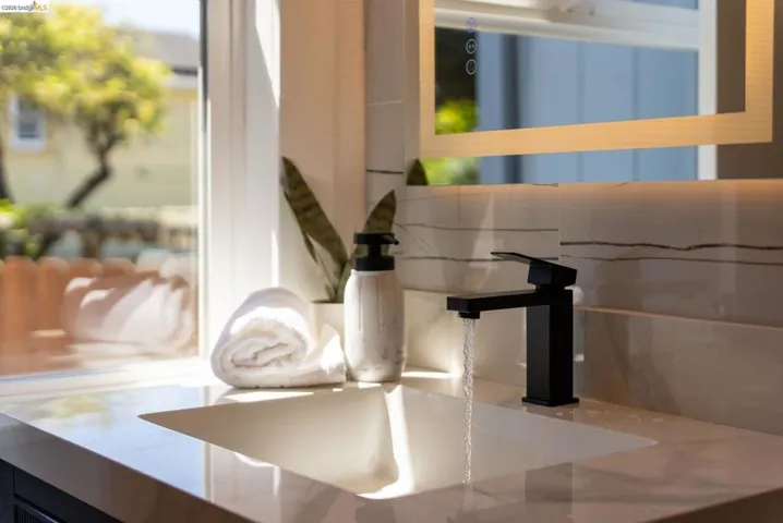 Integrated sink with a polished countertop, matte black faucet, illuminated mirror, and a tile backsplash