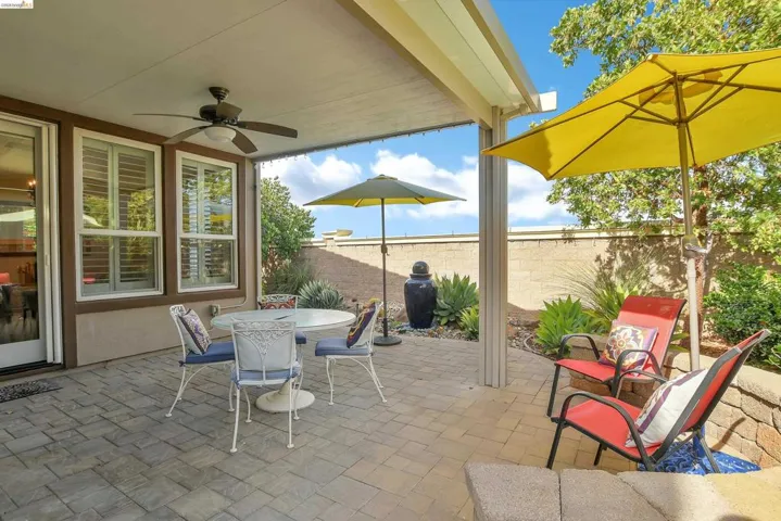 Covered outdoor patio featuring paver flooring, a ceiling fan, and multiple windows with plantation shutters