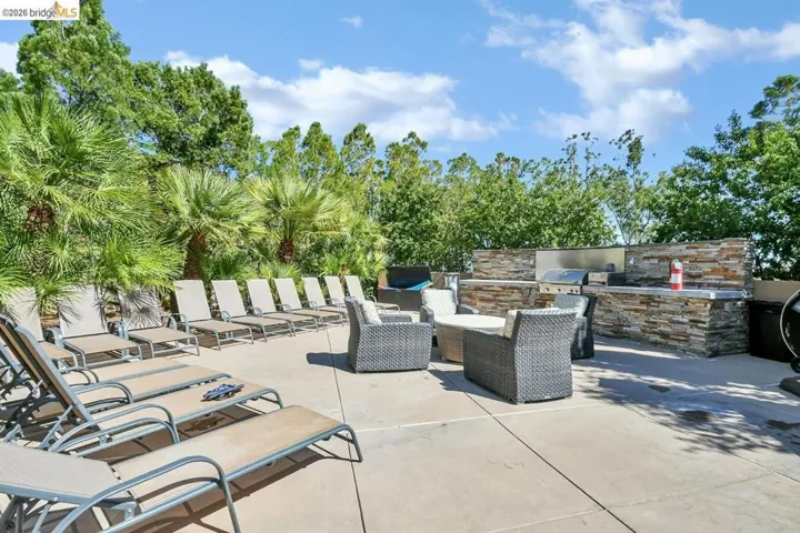 Expansive outdoor patio featuring an integrated stacked stone outdoor kitchen with built-in appliances, ample lounge seating, and lush mature landscaping