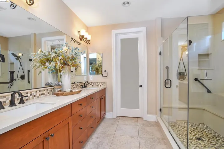 Bathroom featuring a dual vanity with light-colored countertops, dark bronze fixtures, a full-width mirror, and a tiled backsplash