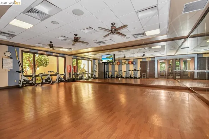 Spacious fitness area featuring wood-finish flooring, full-wall mirrors, and a row of cardio machines