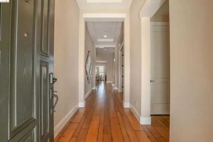 Entryway featuring a paneled front door with dark hardware, wood-finish flooring, light neutral wall paint, white baseboards, and a recessed ceiling with crown molding