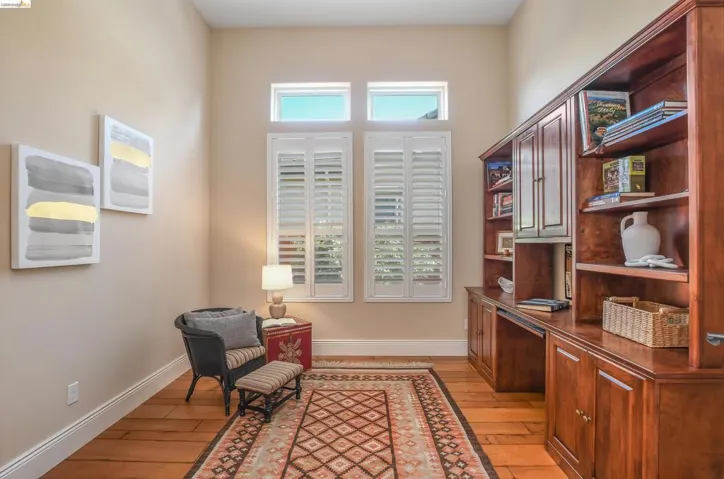 Office space featuring hardwood flooring, extensive built-in custom cabinetry, window shutters, and a high ceiling