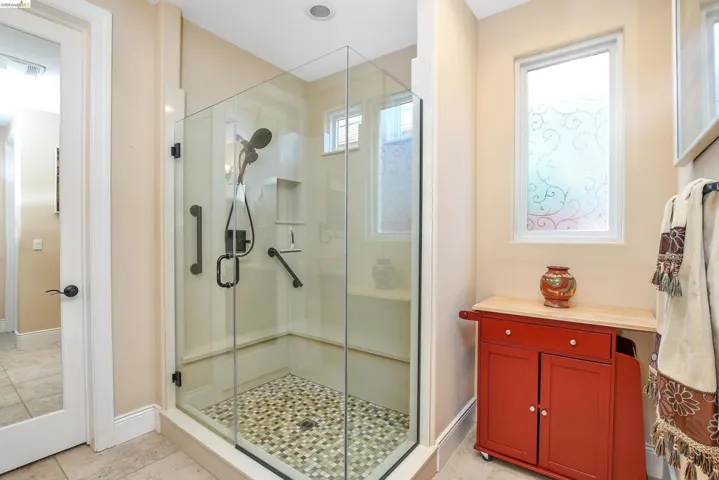 Glass-enclosed shower with pebble-tile flooring, integrated shelving, and a built-in bench