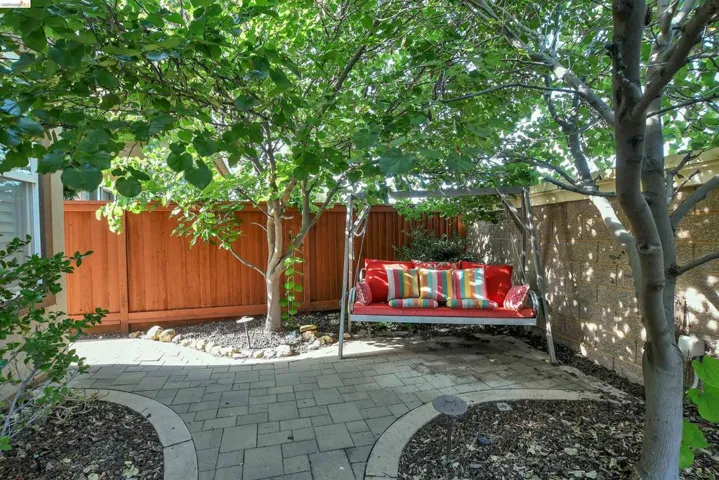 Outdoor patio featuring paver stone flooring with a curved border, mature trees providing natural shade, a wood privacy fence, and an exterior wall constructed of concrete blocks