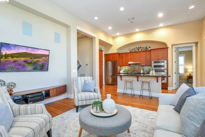 Open-concept living area featuring wood-finish flooring, recessed lighting, a built-in media console, and an integrated kitchen with stainless steel appliances
