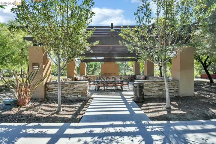 Expansive outdoor gathering area featuring a large pergola, built-in fireplace, stone veneer accents, and mature trees