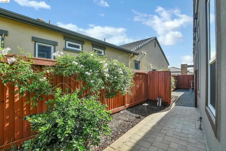 Paver patio walkway alongside a richly stained wooden fence, adorned with climbing green foliage