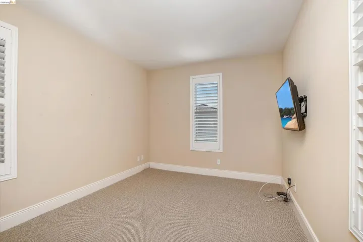 Carpeted room featuring neutral wall tones, white trim, and two windows with white plantation shutters