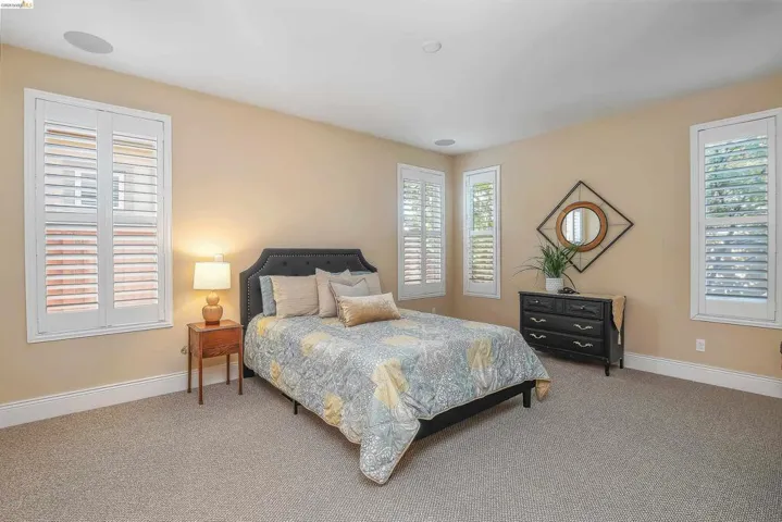 Carpeted interior space featuring multiple windows with plantation shutters, in-ceiling speakers, and neutral wall tones