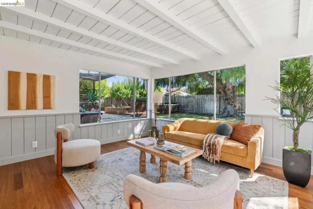 Bright living space featuring exposed white ceiling beams, rich wood-finish flooring, and wainscoting
