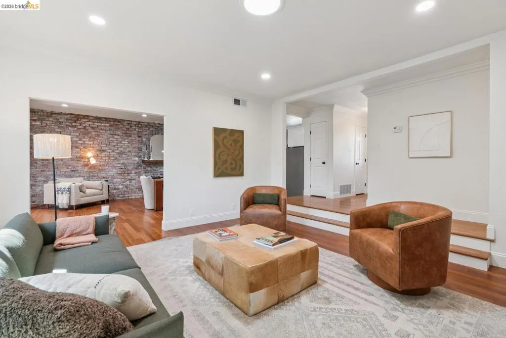 Living area featuring recessed lighting, hardwood flooring, an exposed brick accent wall, white baseboards, and white trim