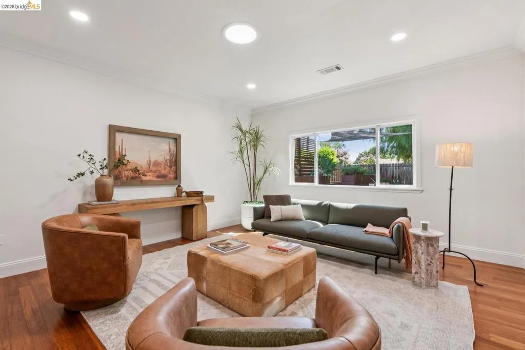 Living space featuring wood-finish flooring, a large window, recessed lighting, crown molding, and a skylight