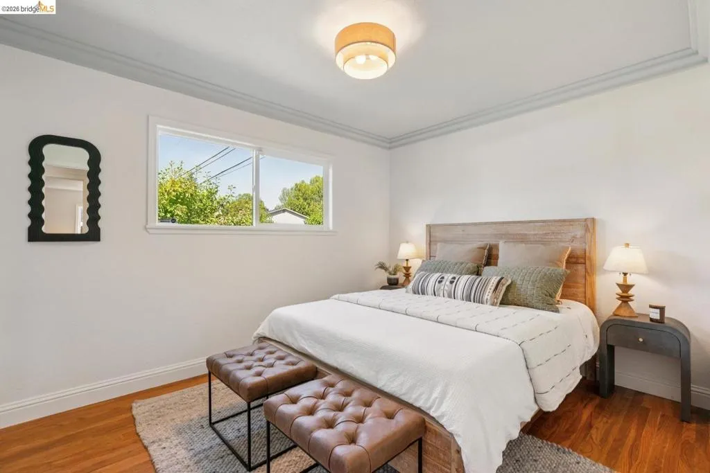 Bedroom featuring hardwood flooring, a large window, crown molding, a built-in light fixture, and a wooden headboard