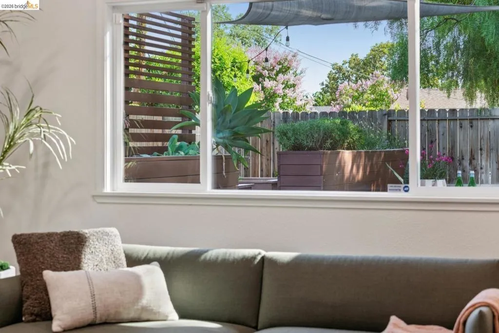 Sliding glass windows overlooking a backyard with wood planter boxes, a slatted privacy screen, and mature landscaping