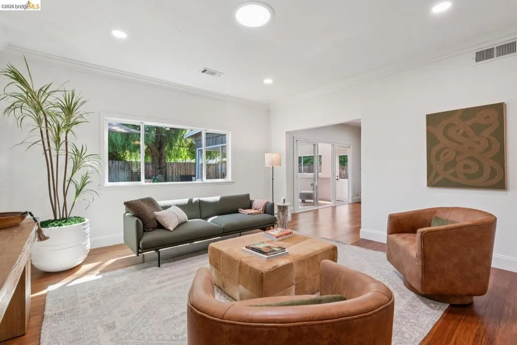 Bright living space featuring warm wood-finish flooring, recessed lighting, a skylight, crown molding, and a wide window overlooking exterior greenery