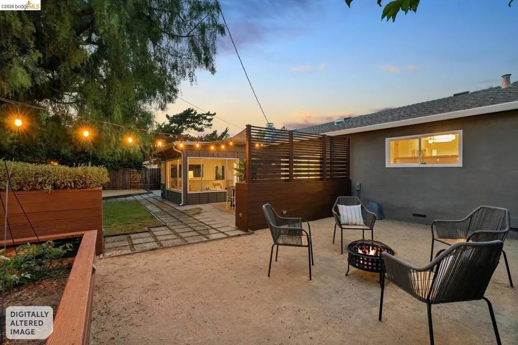 Expansive backyard featuring a gravel patio with string lighting, a detached structure with multiple windows, wood-finish privacy fencing, and wood-finish raised garden beds