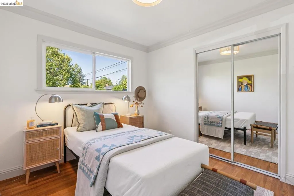Bedroom featuring wood-finish flooring, a double window with a white frame, white crown molding, and a built-in mirrored sliding closet