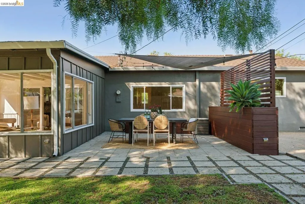 Expansive patio featuring square paver stones, a built-in wood-look planter with slatted privacy screen, and a shade sail overhead