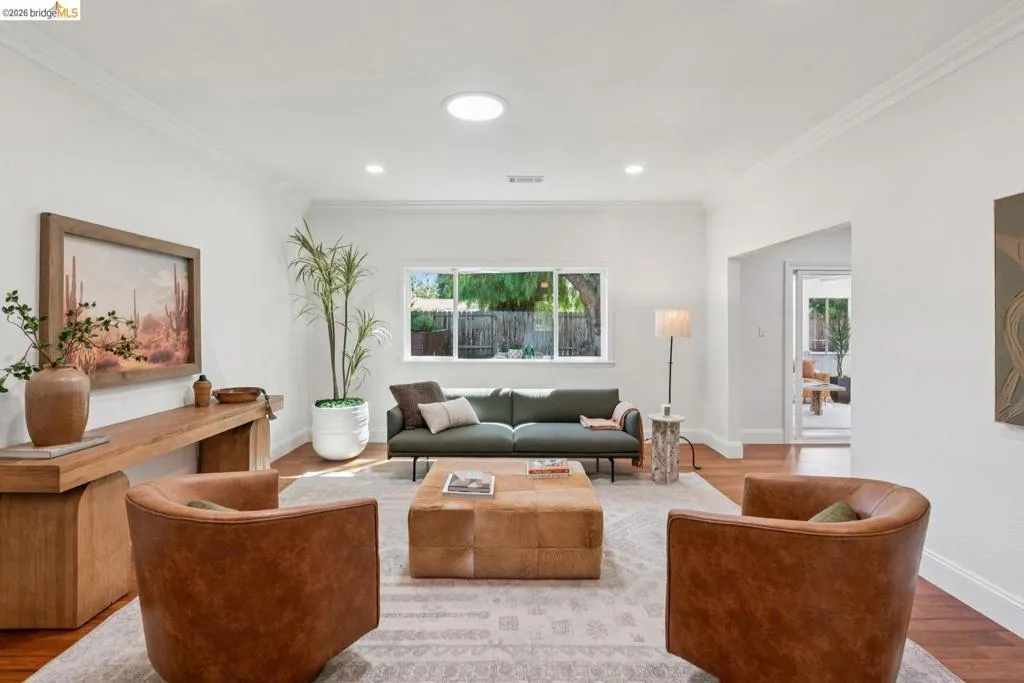 Spacious living area featuring rich wood flooring, crown molding, white painted walls, a large window, and recessed lighting