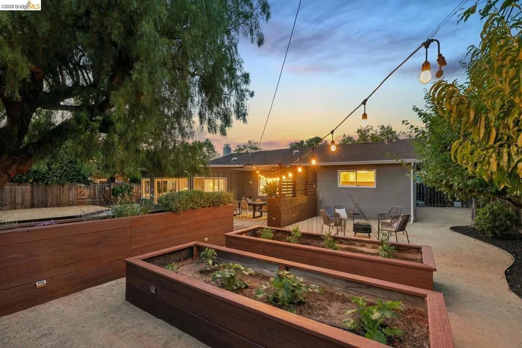 Spacious backyard featuring multiple raised garden beds, a gravel patio, and a dedicated outdoor seating area with string lighting