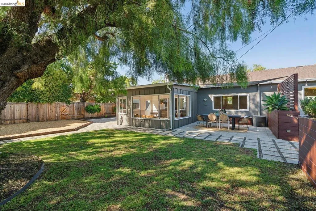 Expansive backyard featuring a manicured lawn, paver patio, and mature tree providing substantial shade