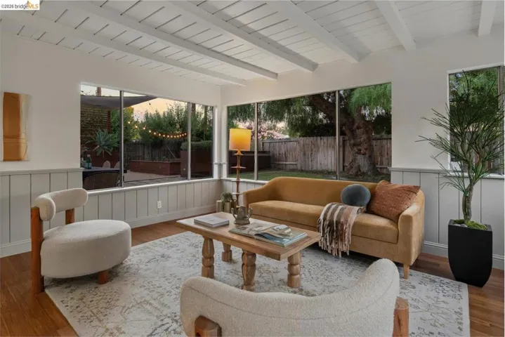 Living area featuring expansive windows, exposed white ceiling beams, light wood-finish flooring, and wainscoting