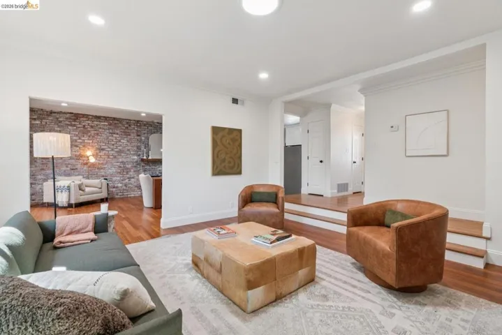 Living area featuring recessed lighting, hardwood flooring, an exposed brick accent wall, white baseboards, and white trim