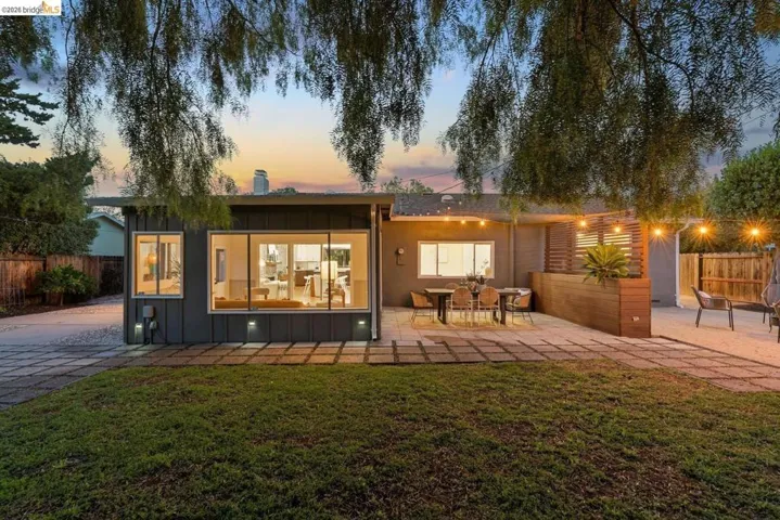 Rear exterior featuring large picture windows, a spacious paved patio, a wood-slat privacy screen, a built-in wood planter, and recessed ground lighting