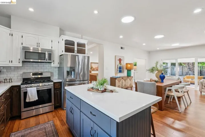 Kitchen featuring a quartz-topped island, stainless steel appliances, subway tile backsplash, and wood-finish flooring
