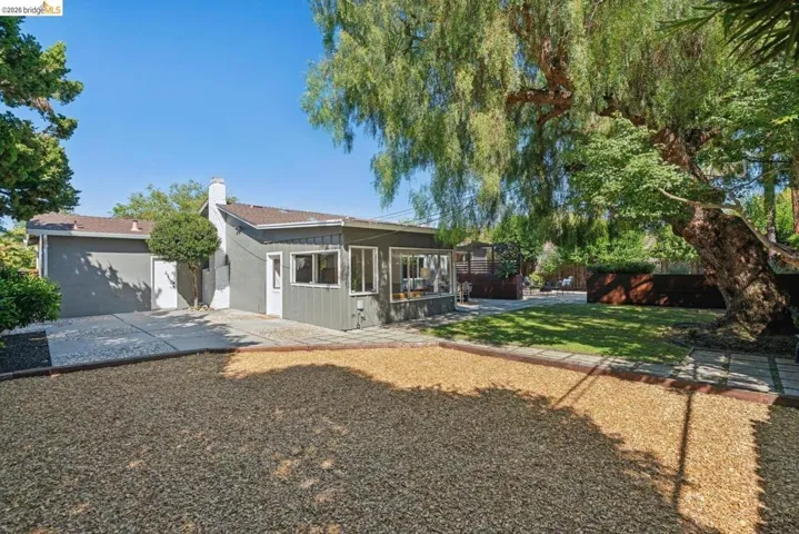 Expansive exterior featuring a gravel patio, green lawn, and mature trees