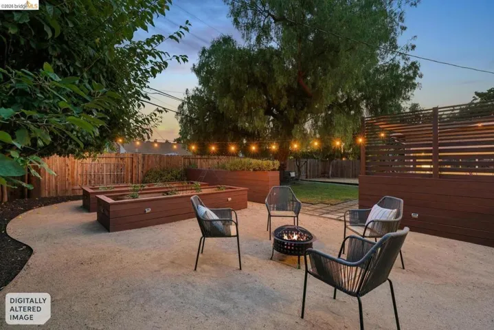 Landscaped backyard featuring multiple raised garden beds, a gravel patio, a fire pit, and string lighting
