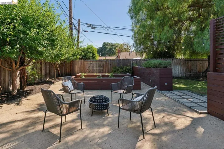 Expansive backyard featuring a pea gravel patio, raised garden beds, a concrete paver pathway, a wooden privacy fence, and mature trees